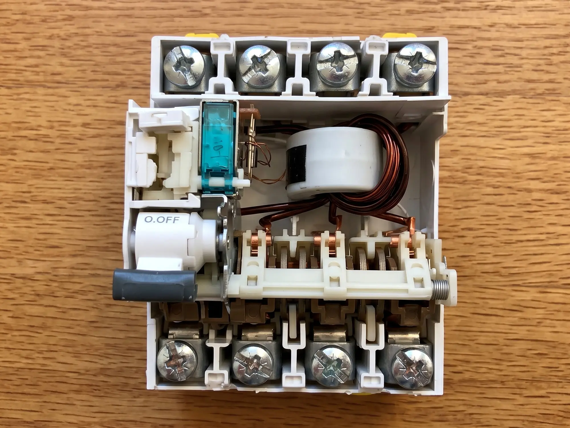 Kaçak akım rölesinin iç yapısı, toroidal transformatörün içinden geçen faz ve nötr kabloları ile tetikleme bobini görünüyor | Levent Elektrik