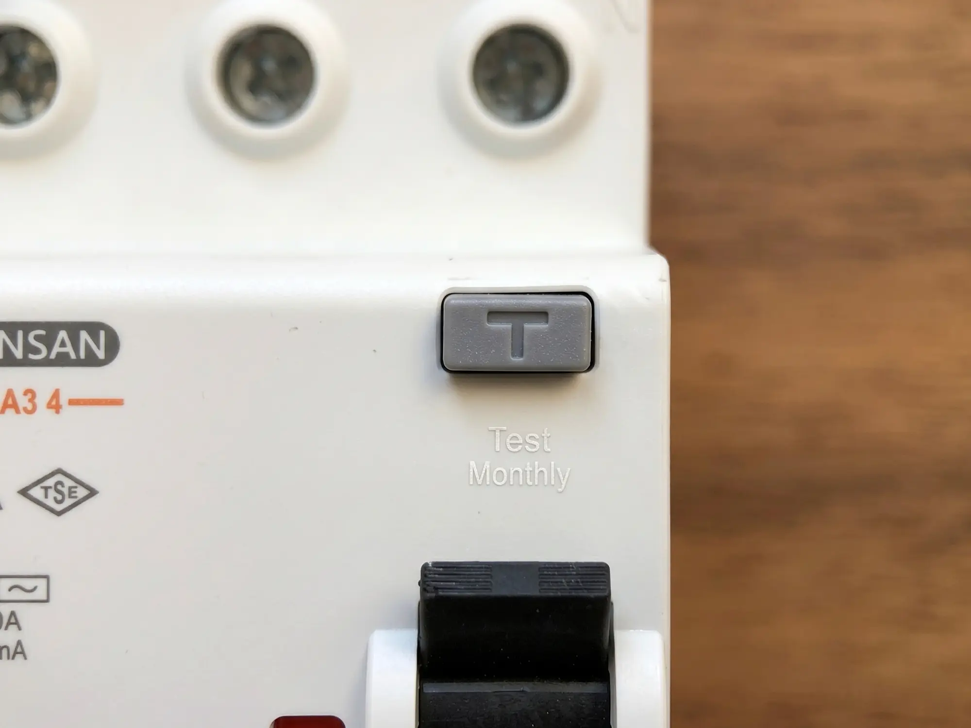 Kaçak akım rölesinin üzerindeki gri T harfi ile işaretlenmiş test butonu ve hassasiyet değeri yakın plan görünüyor | Levent Elektrik