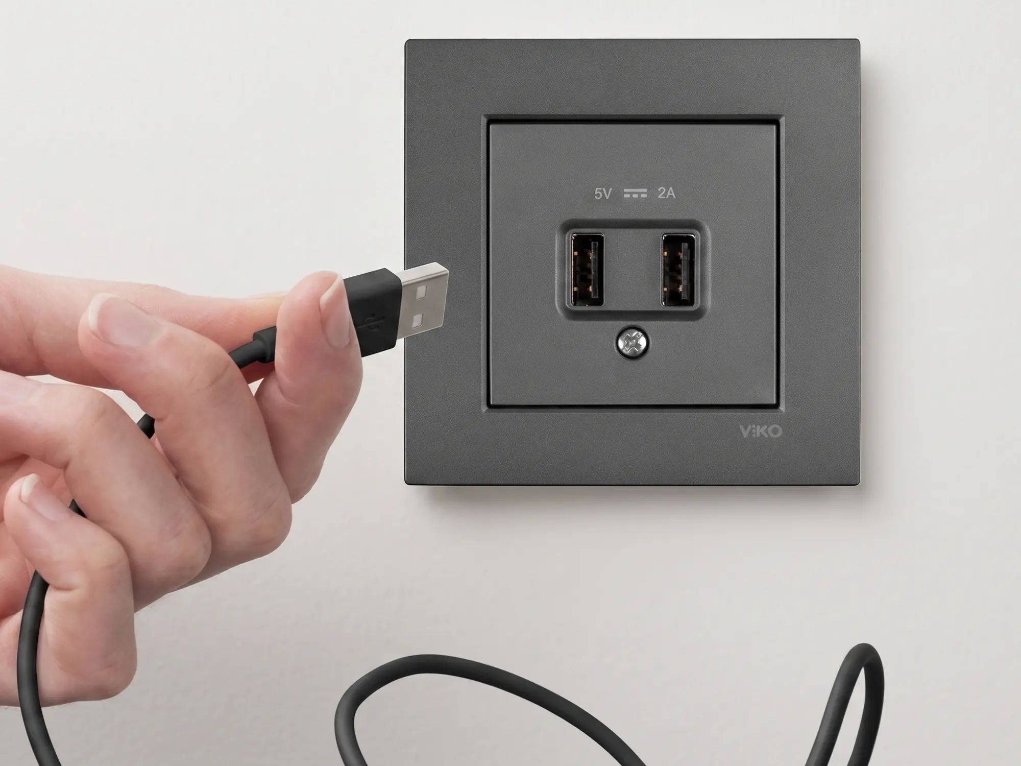 Beyaz duvar yüzeyinde USB-A ve USB-C girişli topraklı priz, telefon şarj kablosu bağlı halde yakın plan görünüyor | Levent Elektrik